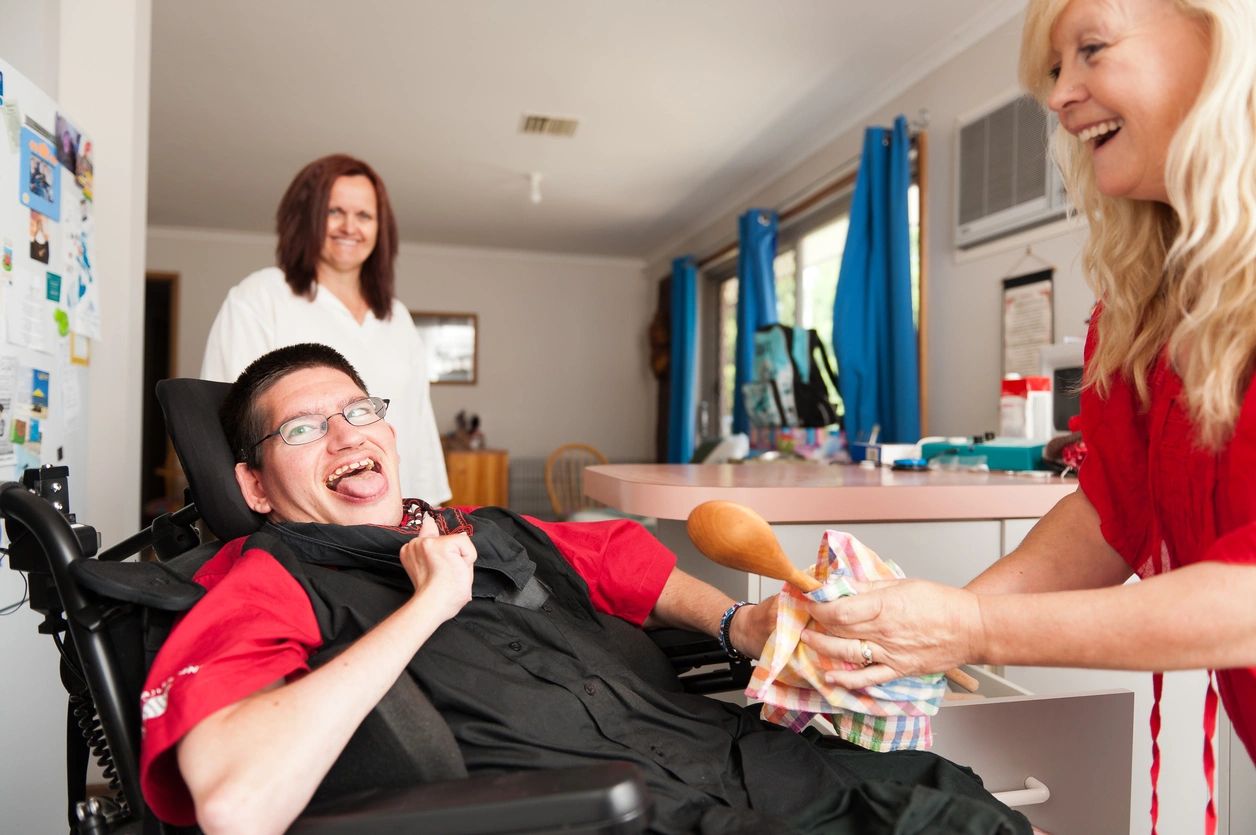 Man in wheelchair laughing with support worker in a care facility